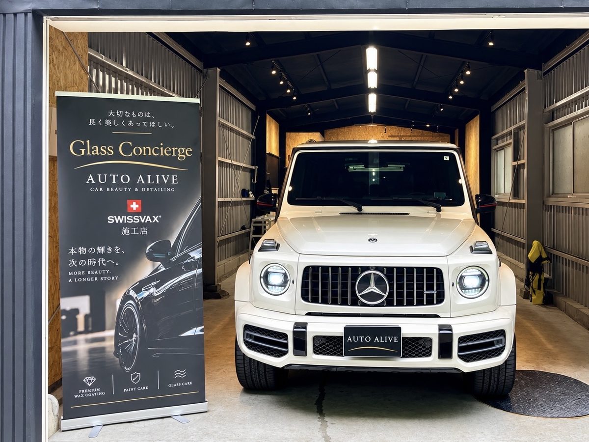 Glass Concierge AUTO ALIVE のガレージに入庫した白いメルセデス・ベンツ Gクラスと店頭バナー